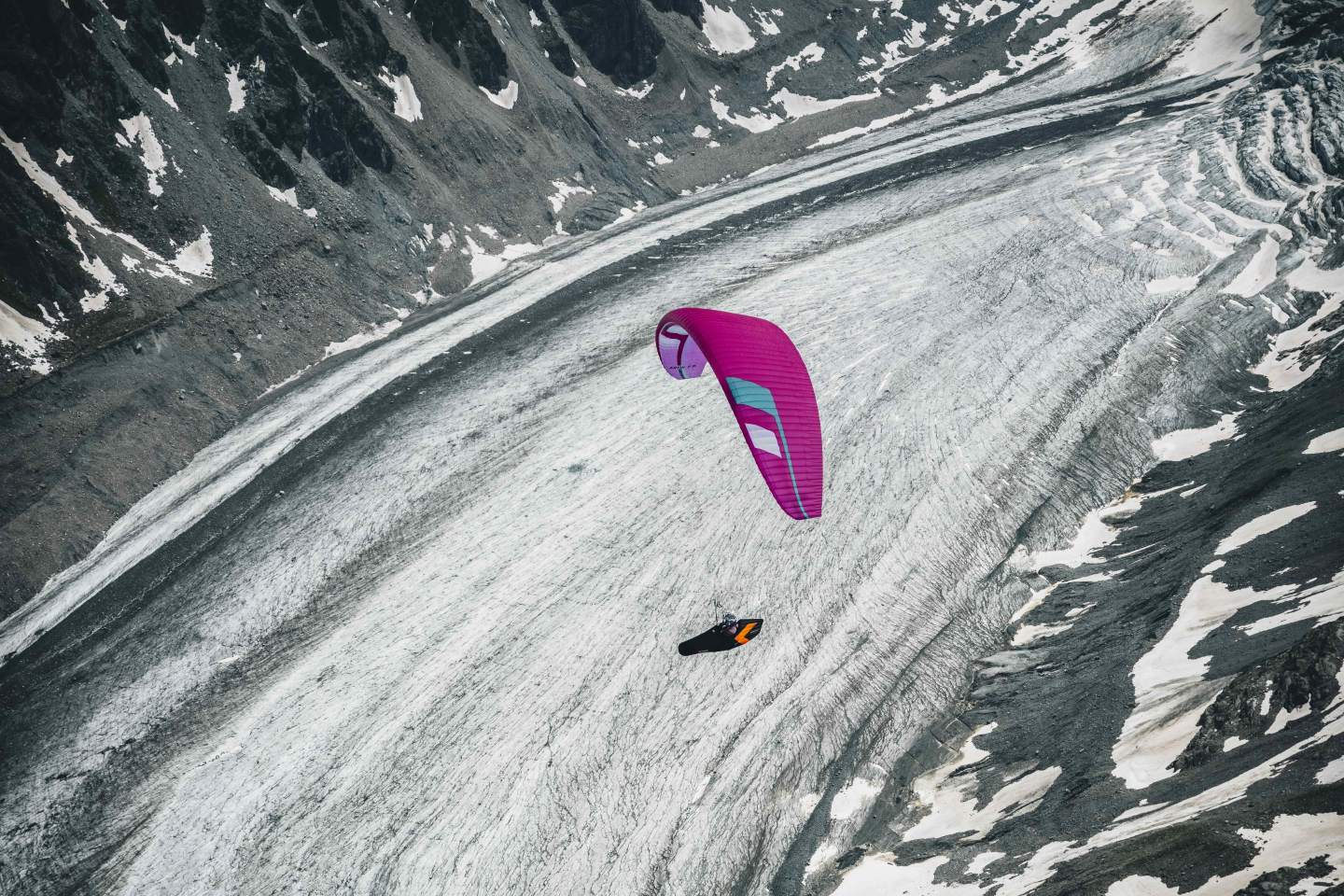Parapente léger aux couleurs vives en vol au-dessus d’un versant de montagne en fin de journée, illustrant les régimes de vent d’un vol hike & fly.