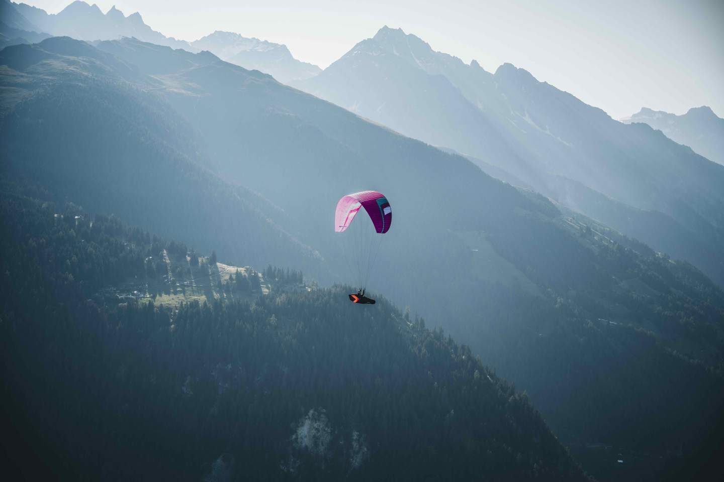 Parapentiste en vol au-dessus d’un relief de montagne, aile ouverte dans un ciel dégagé, illustrant la progression vers le vol en terrain naturel