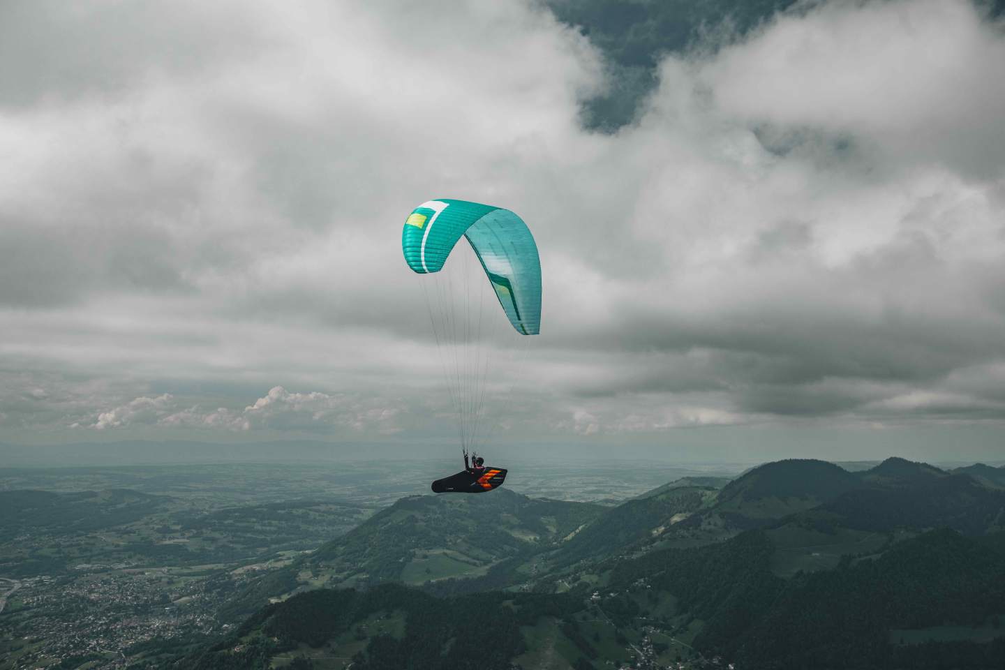 Parapentiste en approche au-dessus d’un relief de moyenne montagne enneigé sous un ciel d’hiver dégagé, voile ouverte plein soleil.
