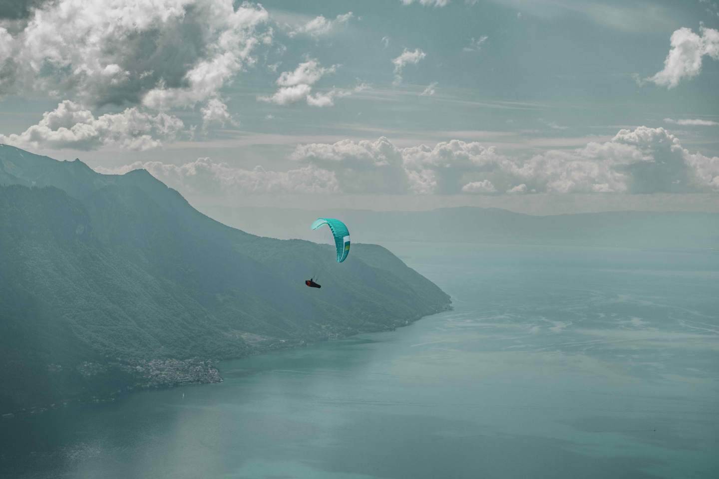 Parapentiste marchant vers un décollage d’altitude au coucher du soleil, sac de bivouac chargé sur le dos, sommets alpins en arrière-plan.