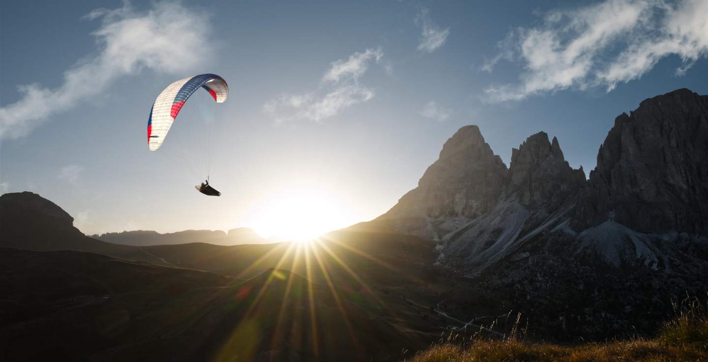 Pilote de parapente en tenue légère progressant sur une crête rocheuse d’altitude, voile pliée sur le dos, dans une lumière de fin de matinée en montagne.