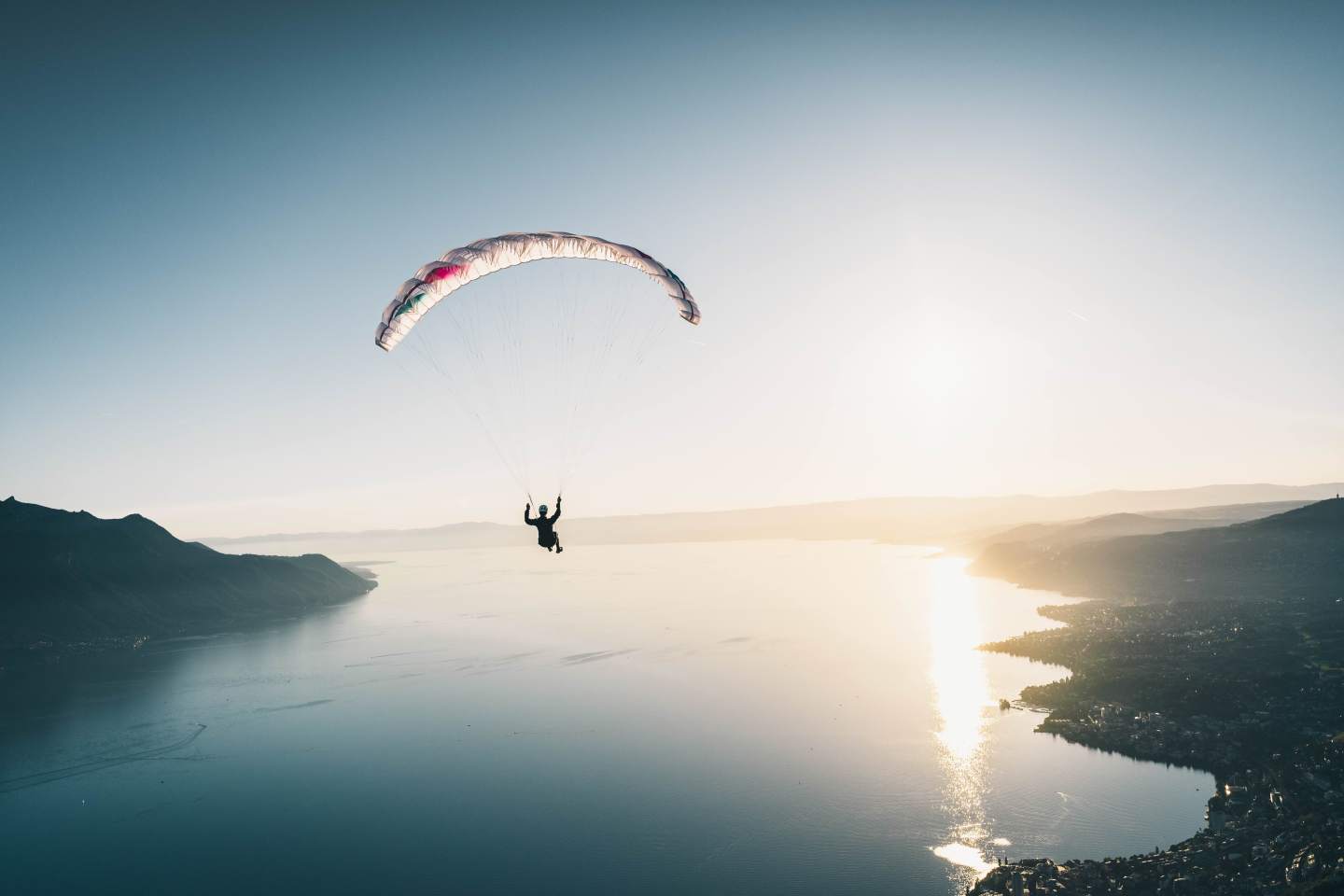 Pilote de parapente en veste isolante au décollage sur un sommet enneigé, aile prête à gonfler