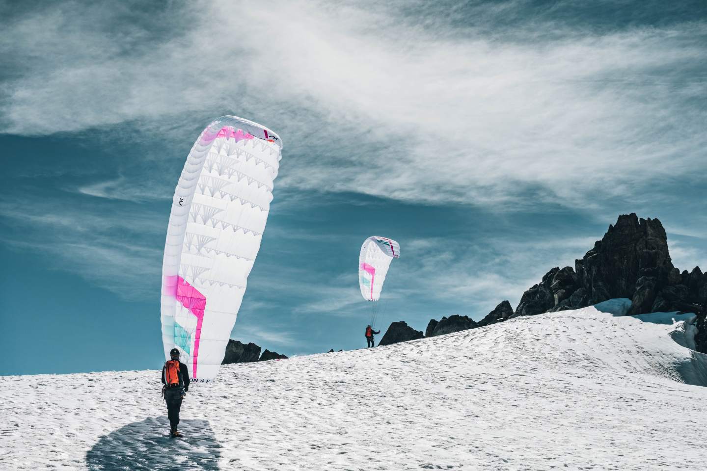 Pilote sur une crête enneigée, sac de portage et voile prêts au décollage
