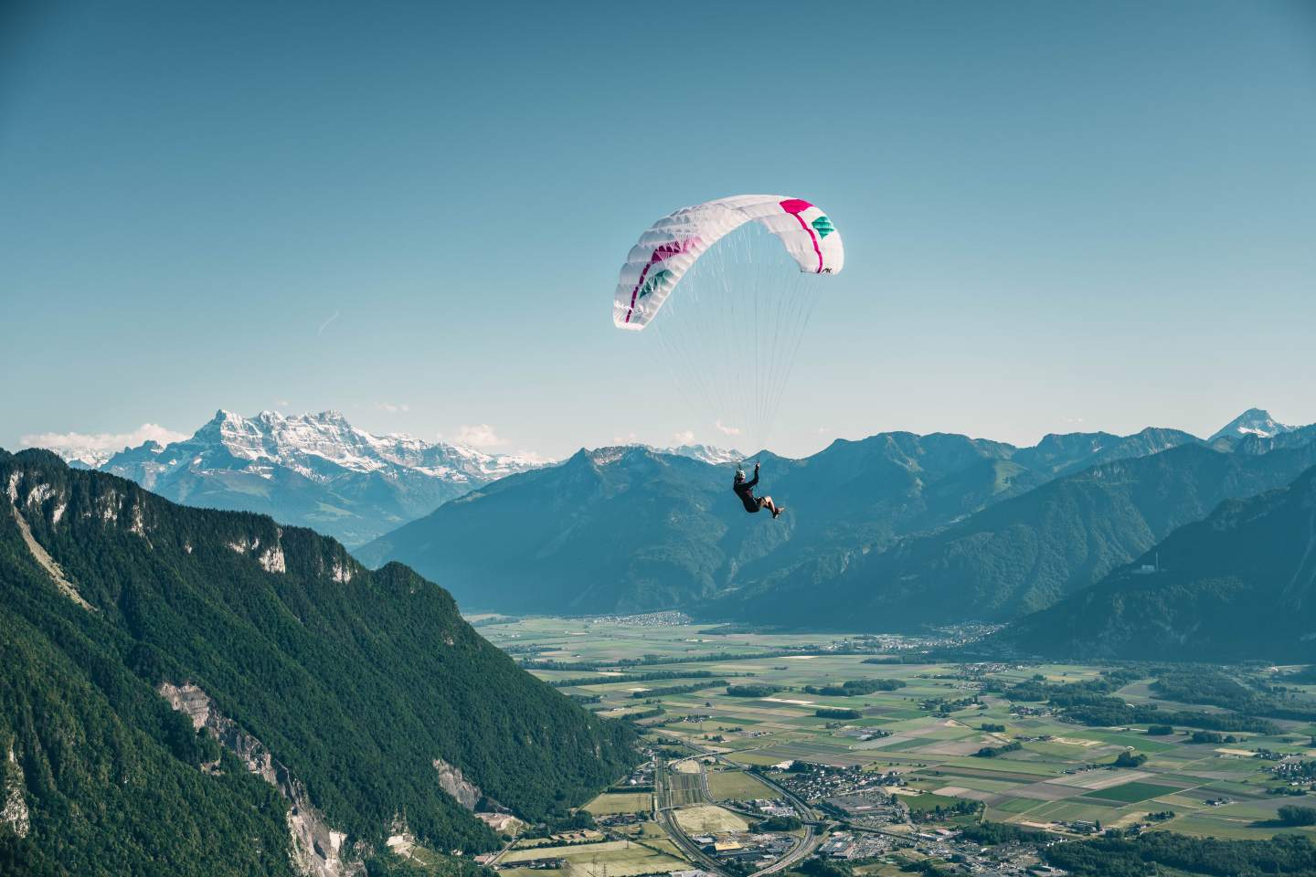 Parapente au-dessus d’une vallée verte face aux sommets enneigés